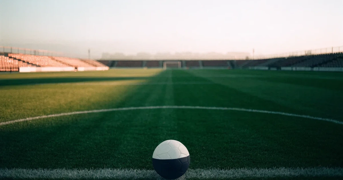 Uma bola de futebol no ponto central de um relvado, à luz da manhã