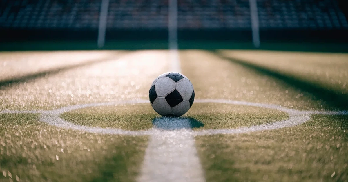 Uma bola de futebol no ponto central de um relvado, à luz da manhã