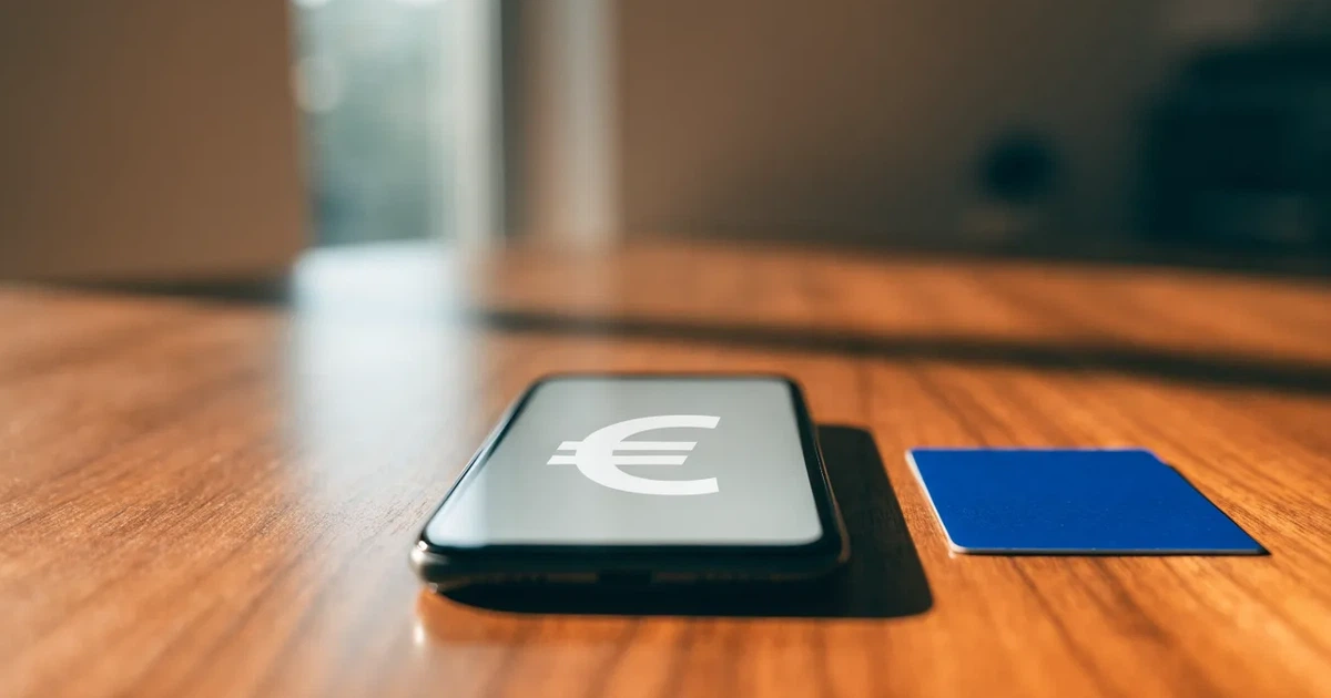 Um telemóvel e um cartão bancário lado a lado numa mesa de madeira, com algumas notas de euro ao lado