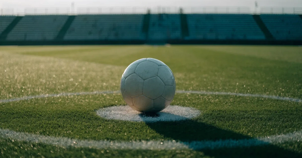 Uma bola de futebol no ponto central de um relvado, à luz da manhã
